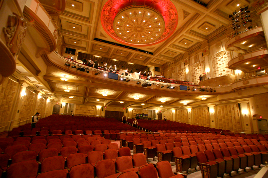 A view of a theatre from the front row looking back, with all the interior lights shining.